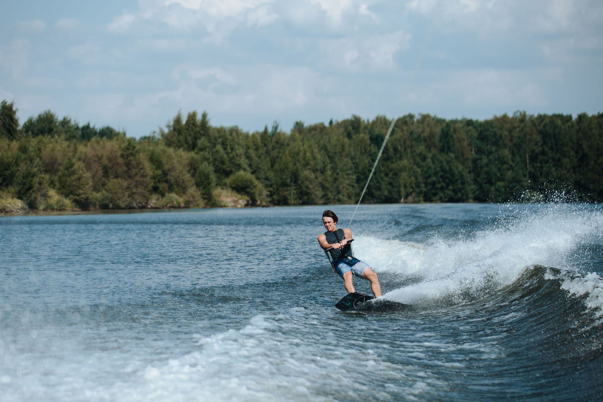 Wakeboarder in a buoyancy vest riding the wake behind a boat on a tree-lined lake