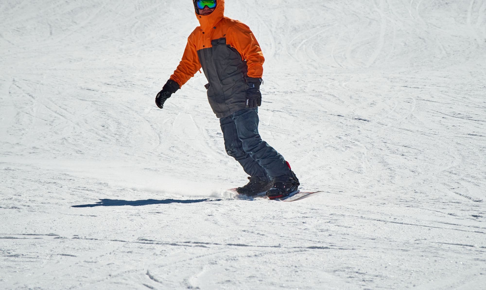 A snowboarder in an orange jacket cruising down a groomed slope