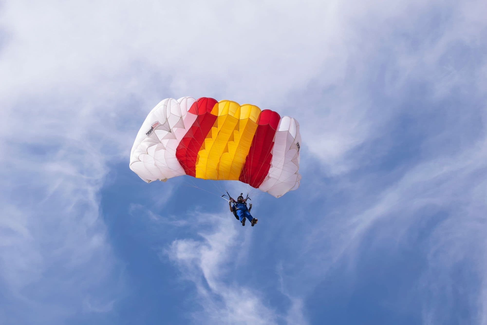 Skydiver under a fully open red, yellow and white canopy in a blue sky