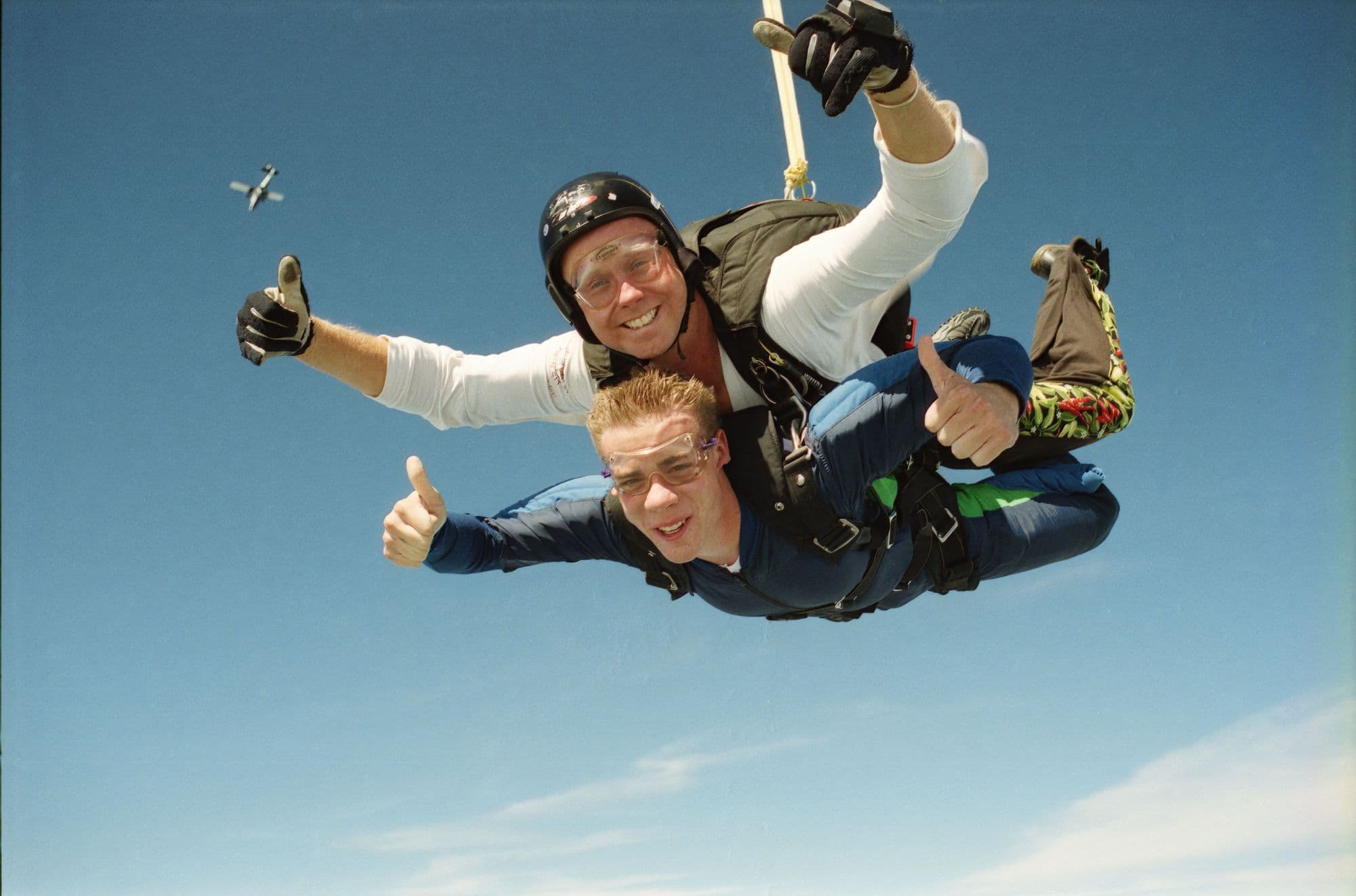 Smiling tandem skydivers in freefall against a blue sky