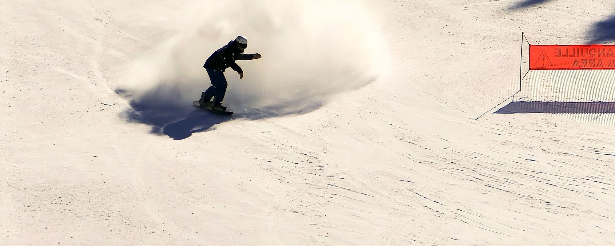 A snowboarder blasting a huge plume of powder on a sunny slope in the French Alps