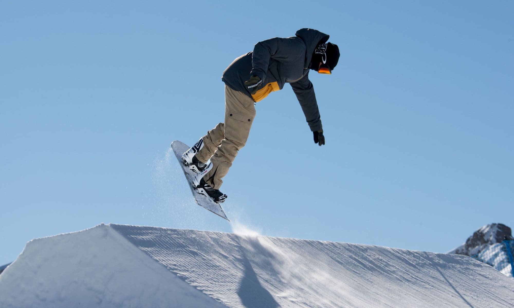 A snowboarder flying high off a park kicker against a deep blue sky in Livigno