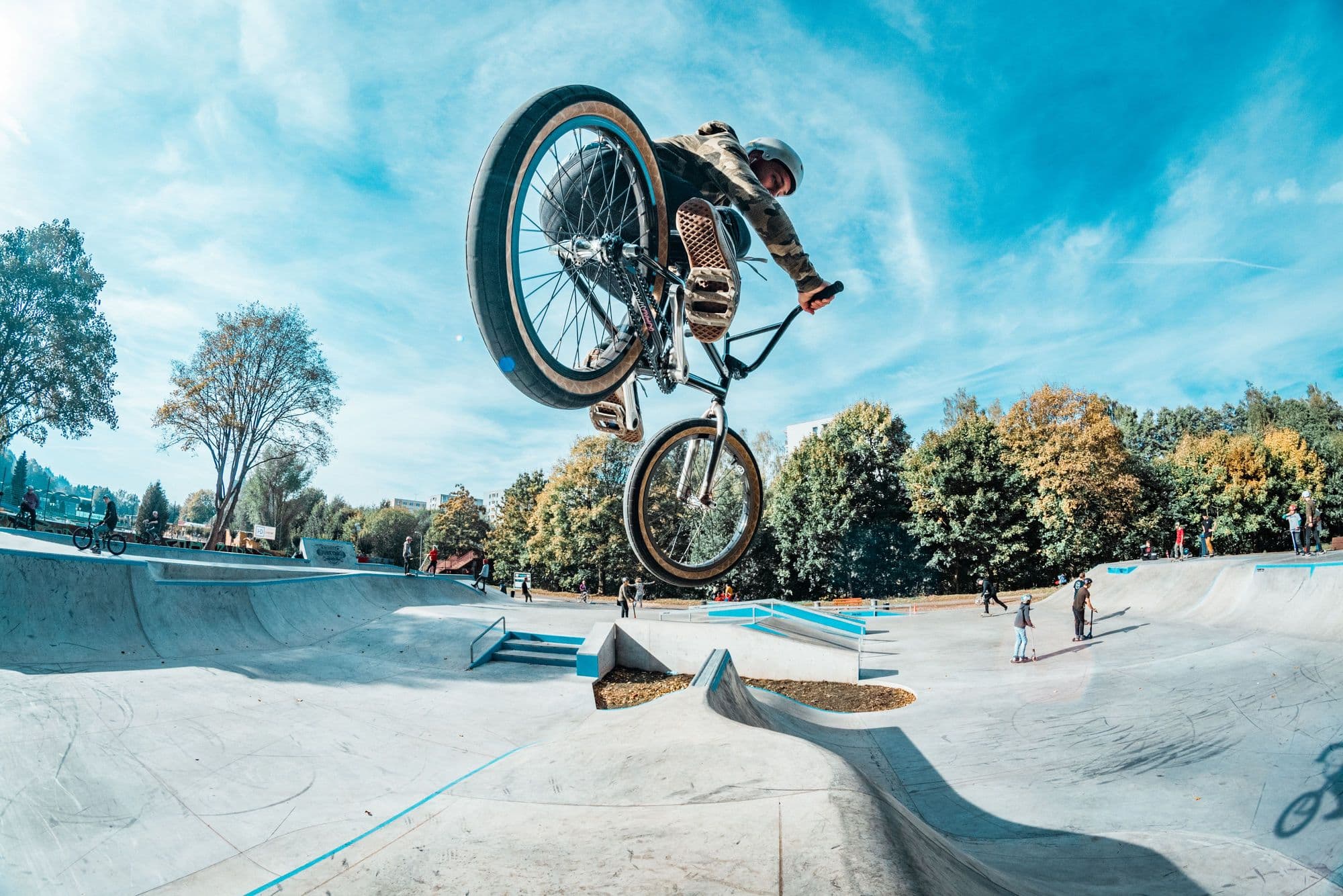 BMX rider in a helmet flying a big air over a sunny concrete skatepark