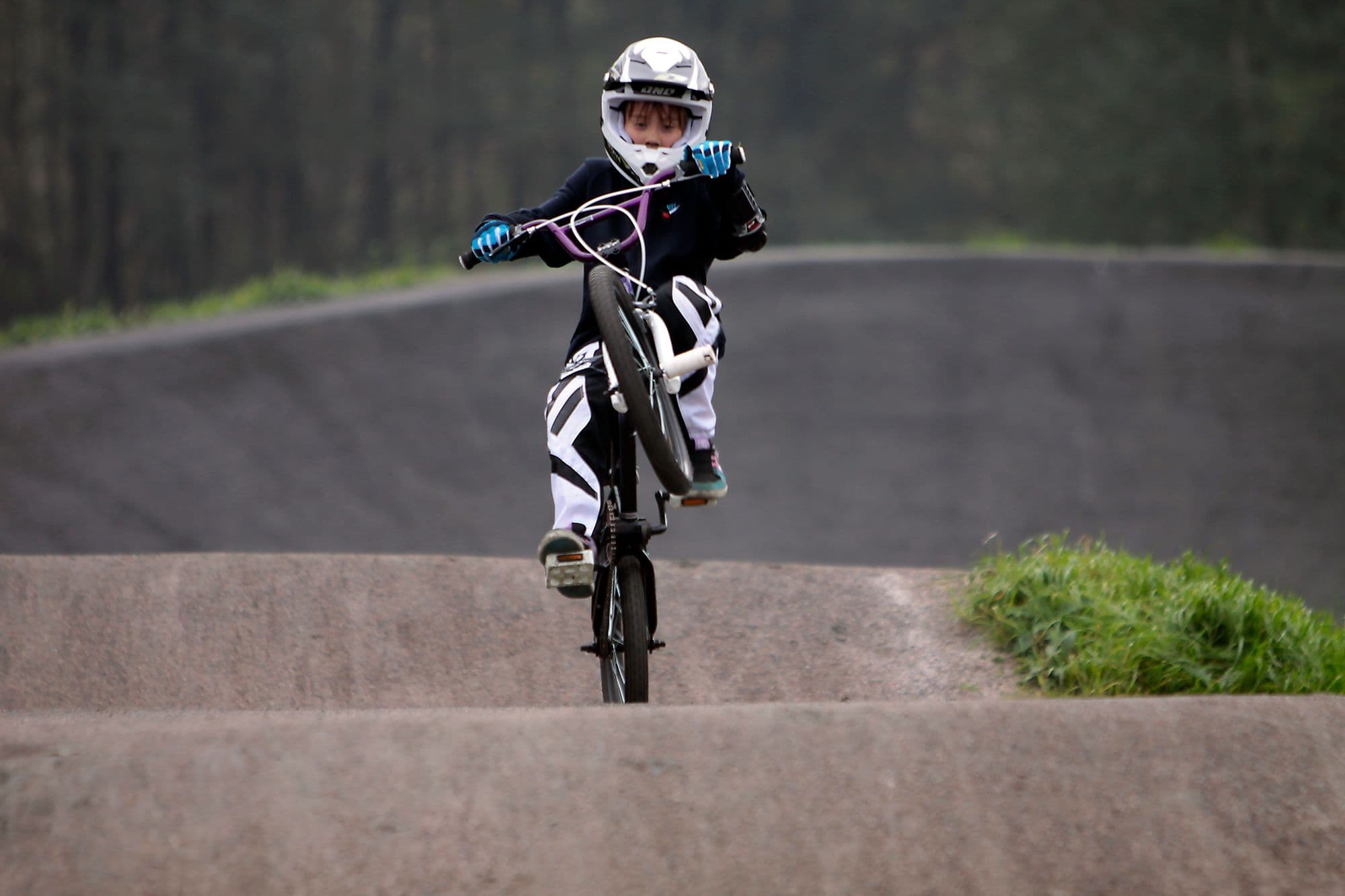 Young BMX racer in helmet and race kit cresting a track jump