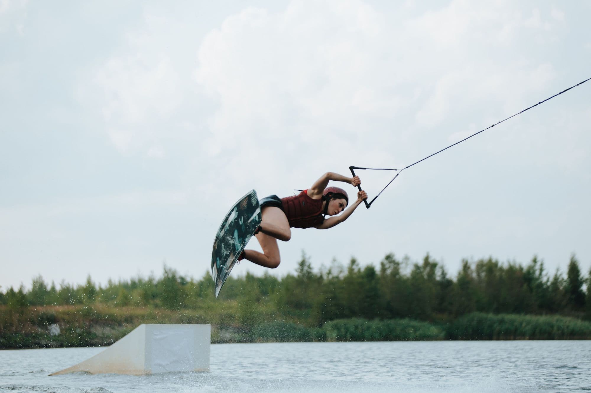 Cable wakeboarder in helmet and vest jumping off a kicker