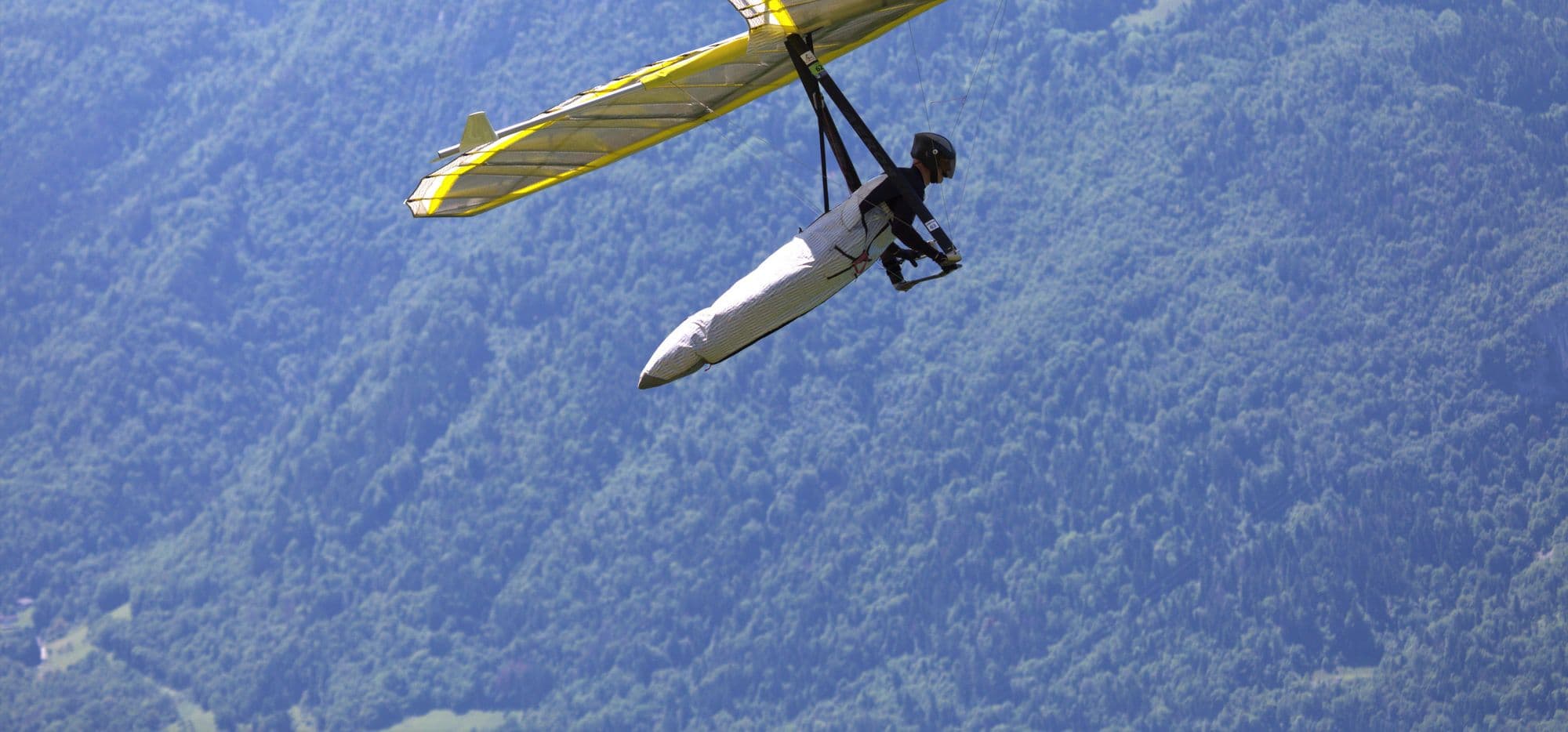 Yellow hang glider racing past a forested mountainside
