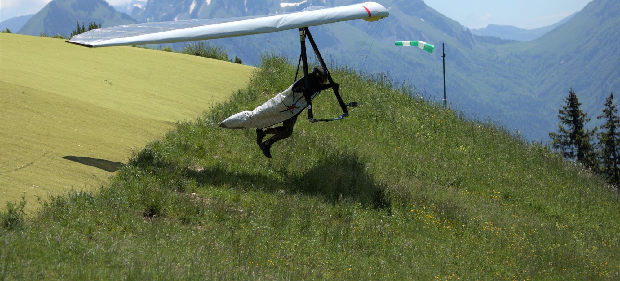 Hang glider lifting off a hillside launch beside a windsock