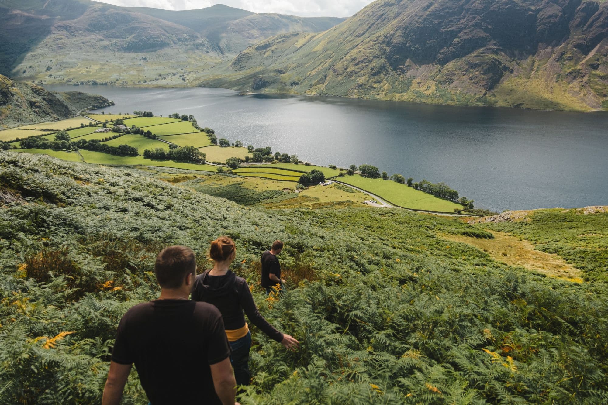 Two walkers heading down a grassy fellside towards a lake