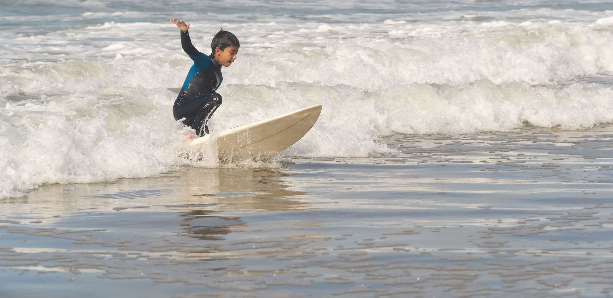 A young surfer standing up and riding whitewater for the first time