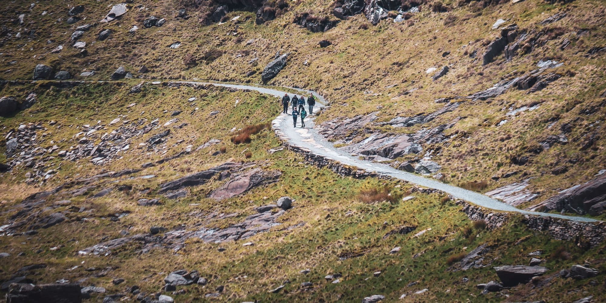 Line of walkers on a stone path through a mountain valley