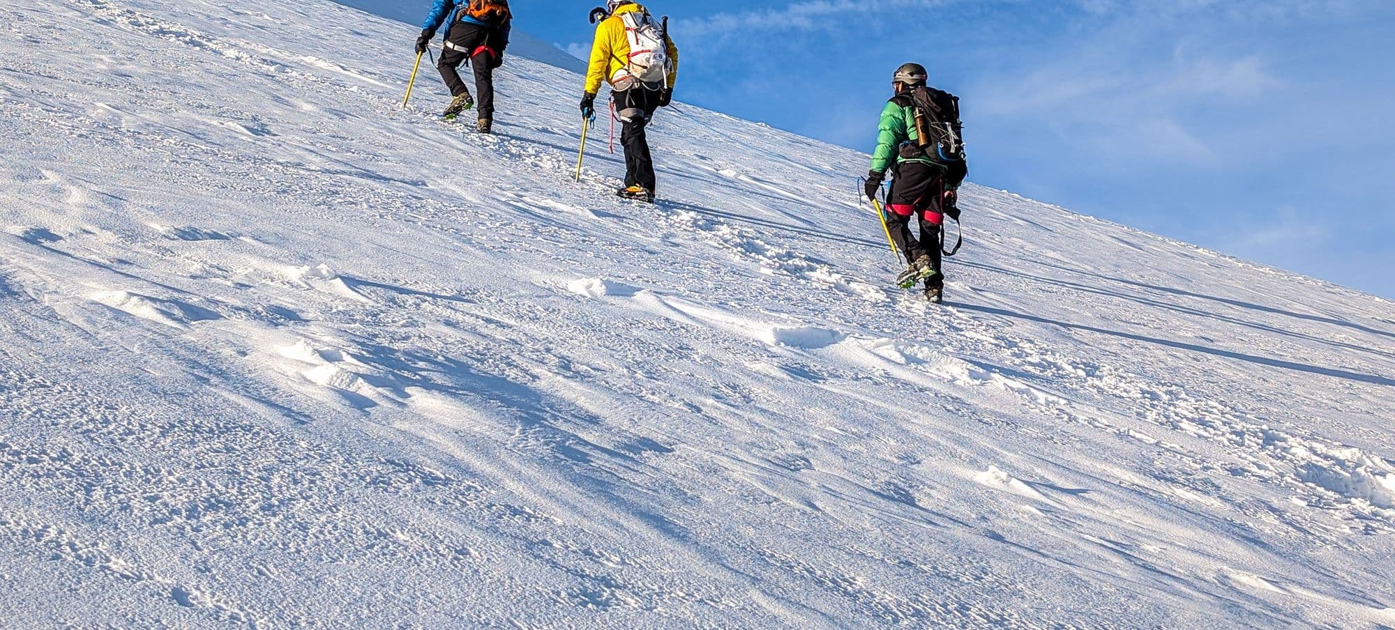 Roped party of mountaineers with ice axes climbing a snowy slope