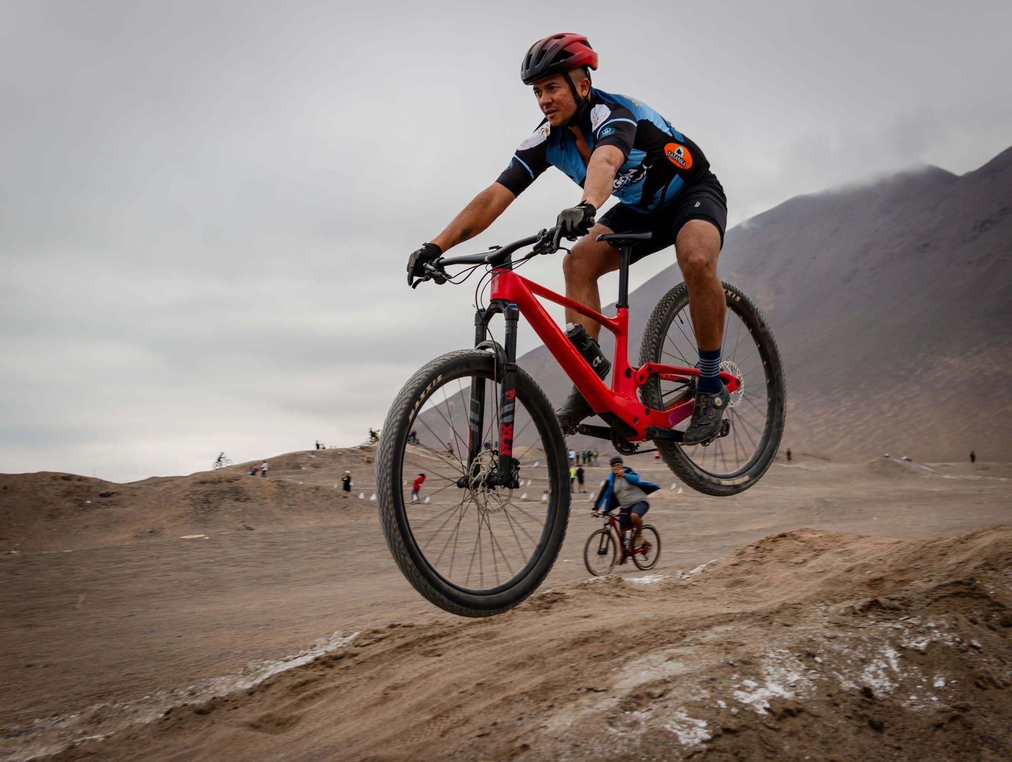 A mountain bike racer in a red helmet jumping a dirt track mid-race