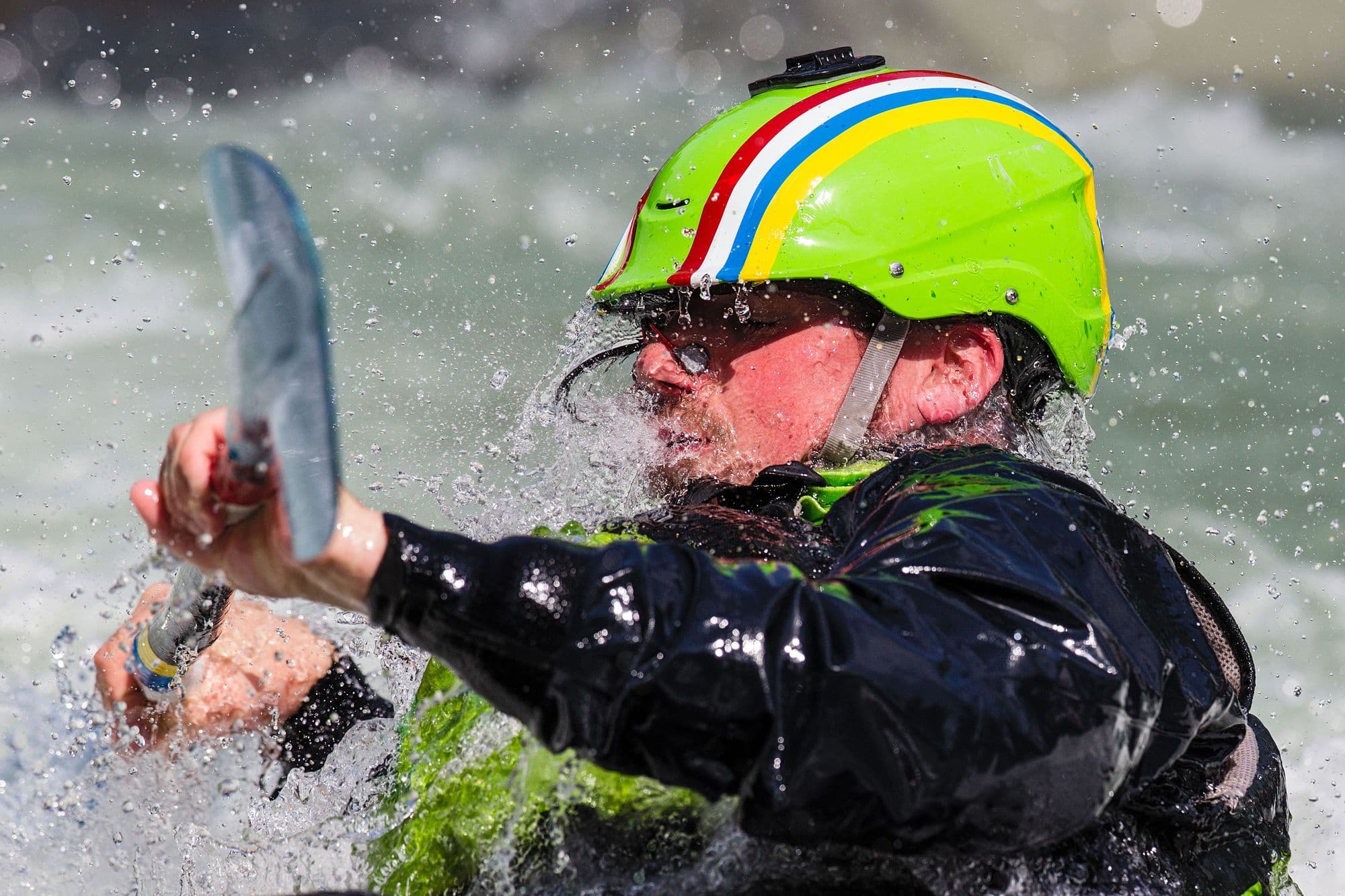 A slalom paddler in a striped helmet punching through spray