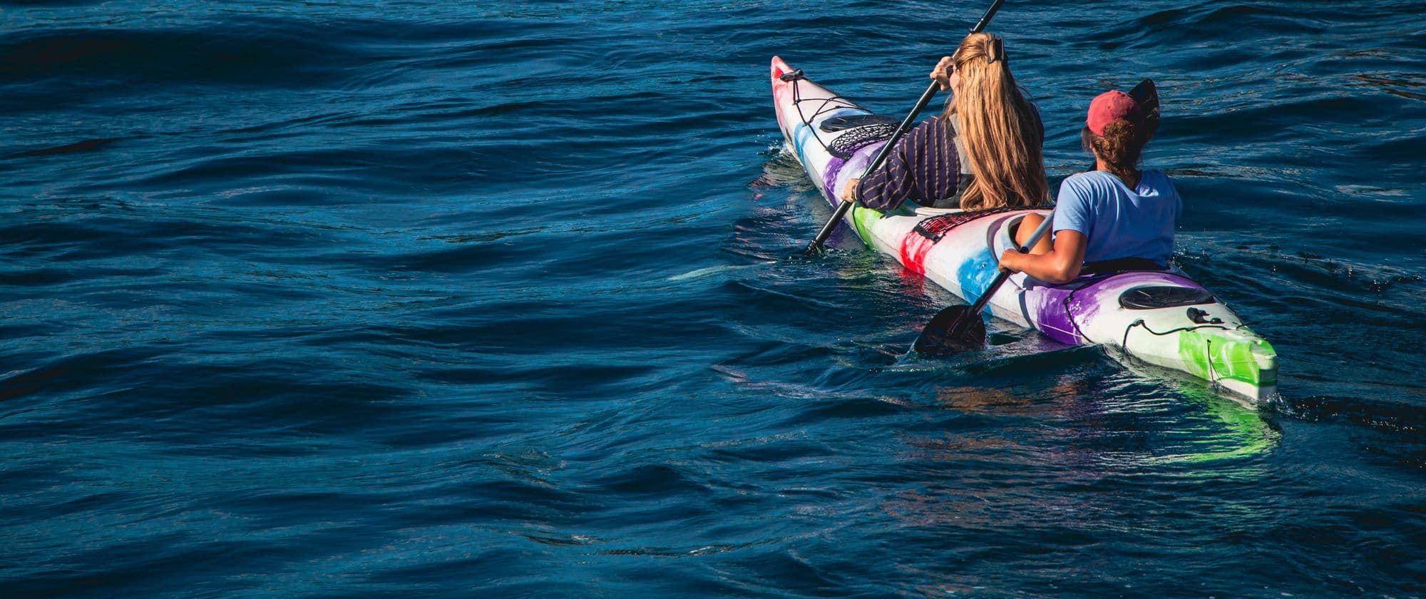 Two smiling paddlers in a colourful kayak on deep blue water