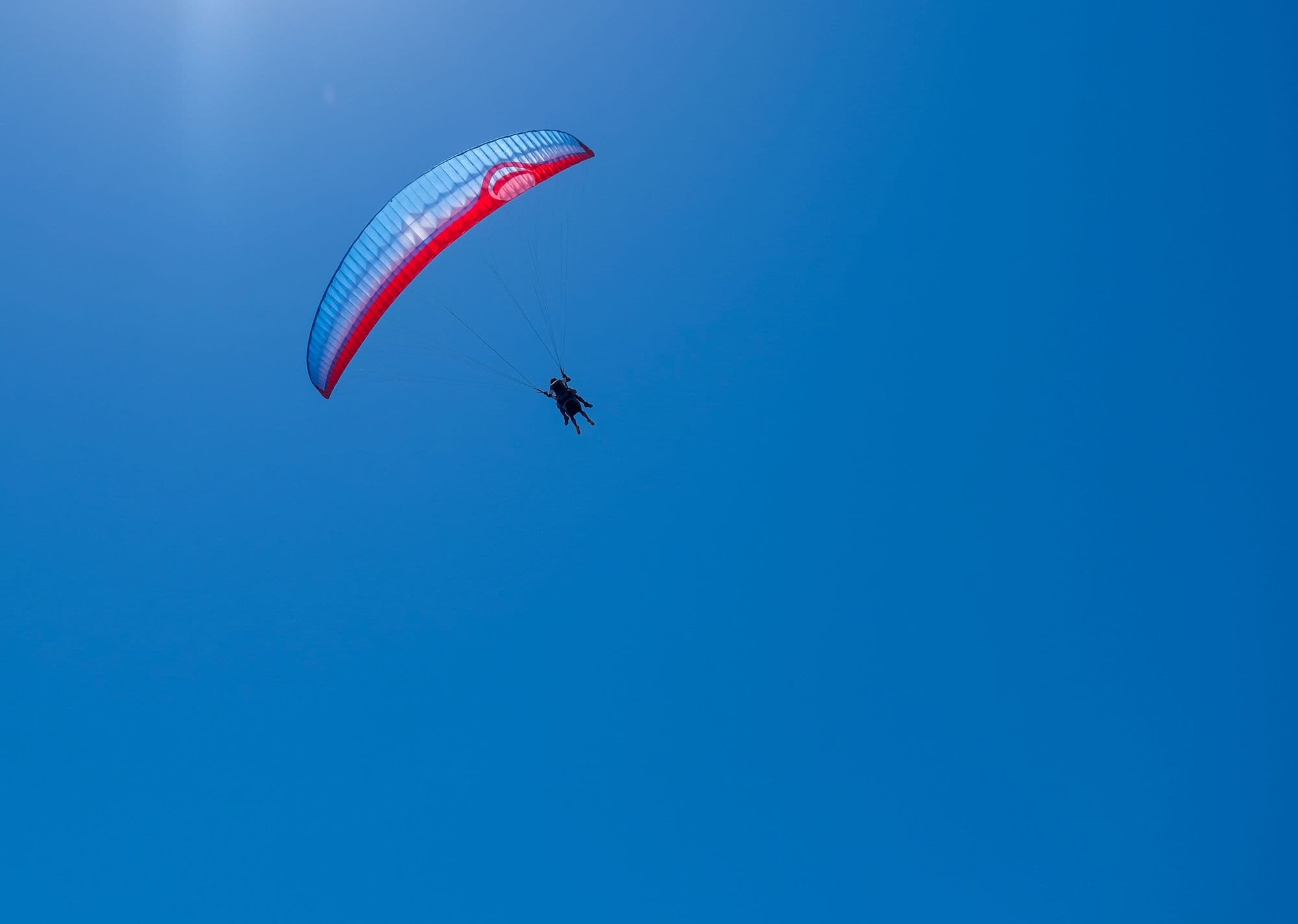 A paraglider under a red and blue wing in a clear blue sky