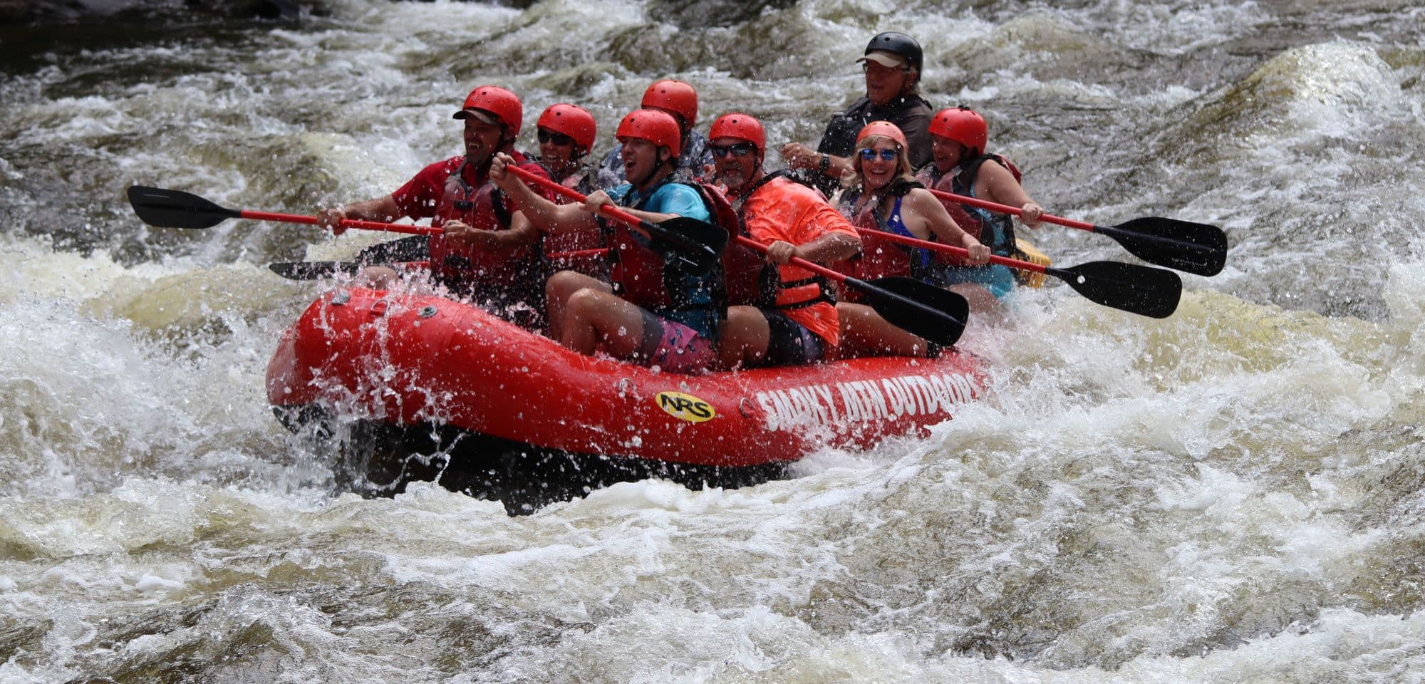 A raft crew in red helmets paddling hard through big rapids