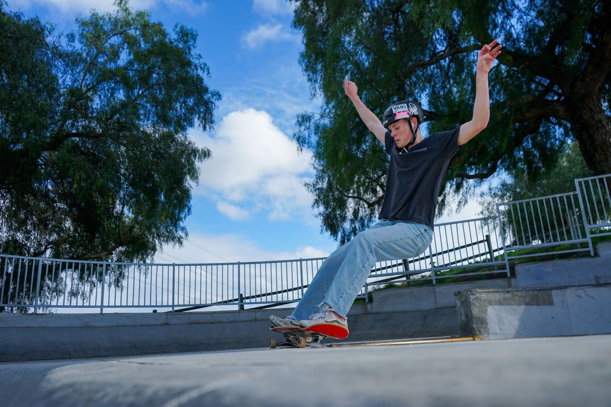 Skater in a helmet grinding a skatepark ledge under blue sky and trees