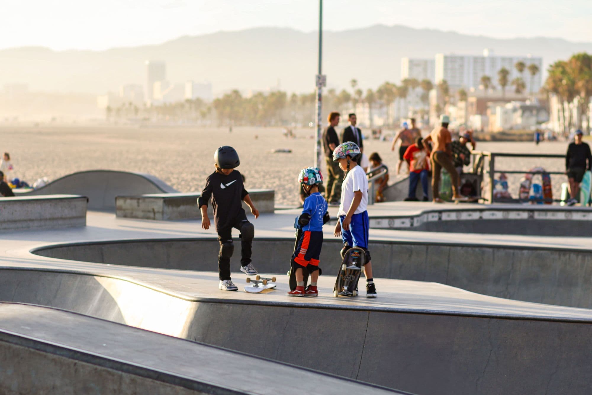 Young skaters in helmets at a busy sunny skatepark