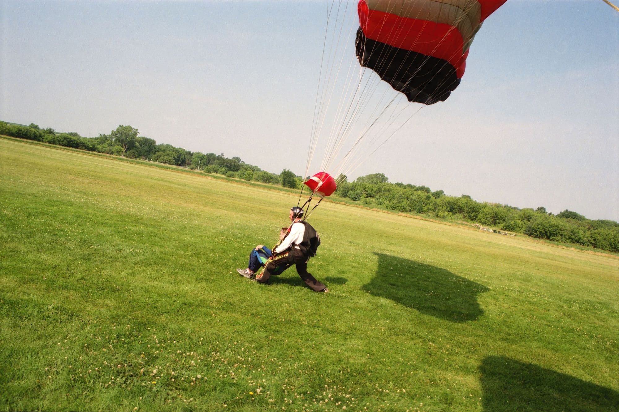 Skydiver landing under canopy on a sunny grass field