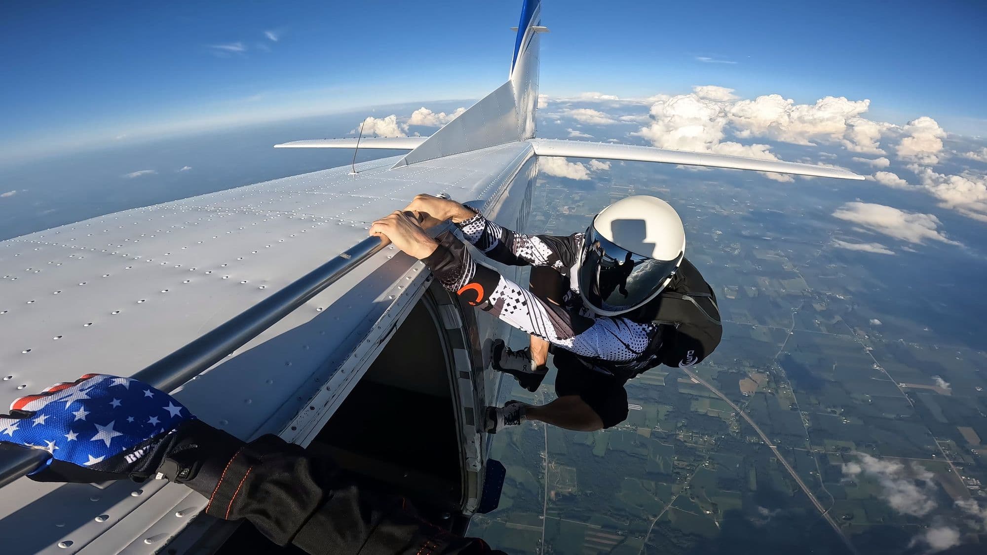 Skydiver gripping the aircraft door ready to jump above the clouds