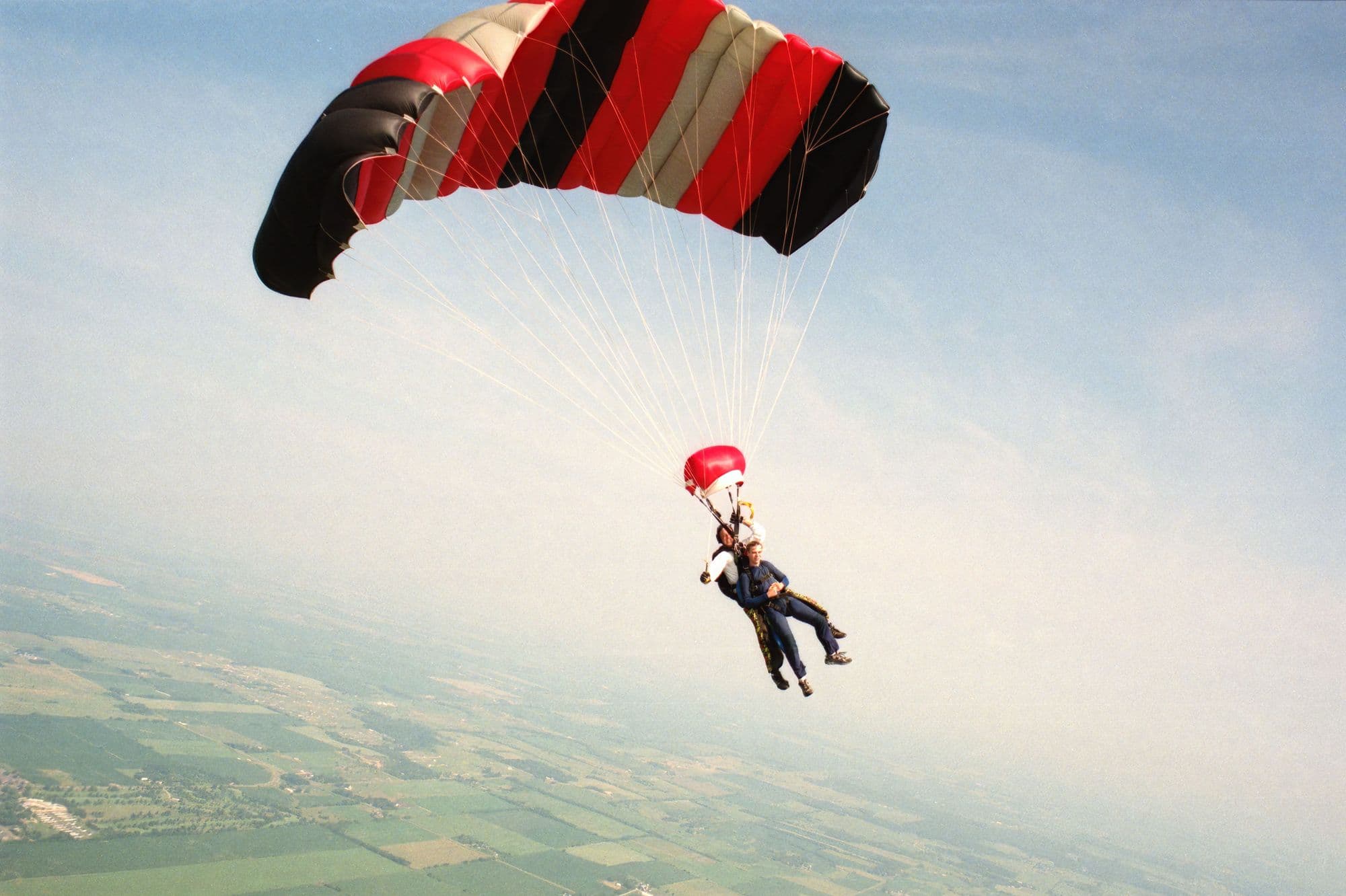 Tandem instructor and student under a red and black canopy in a blue sky