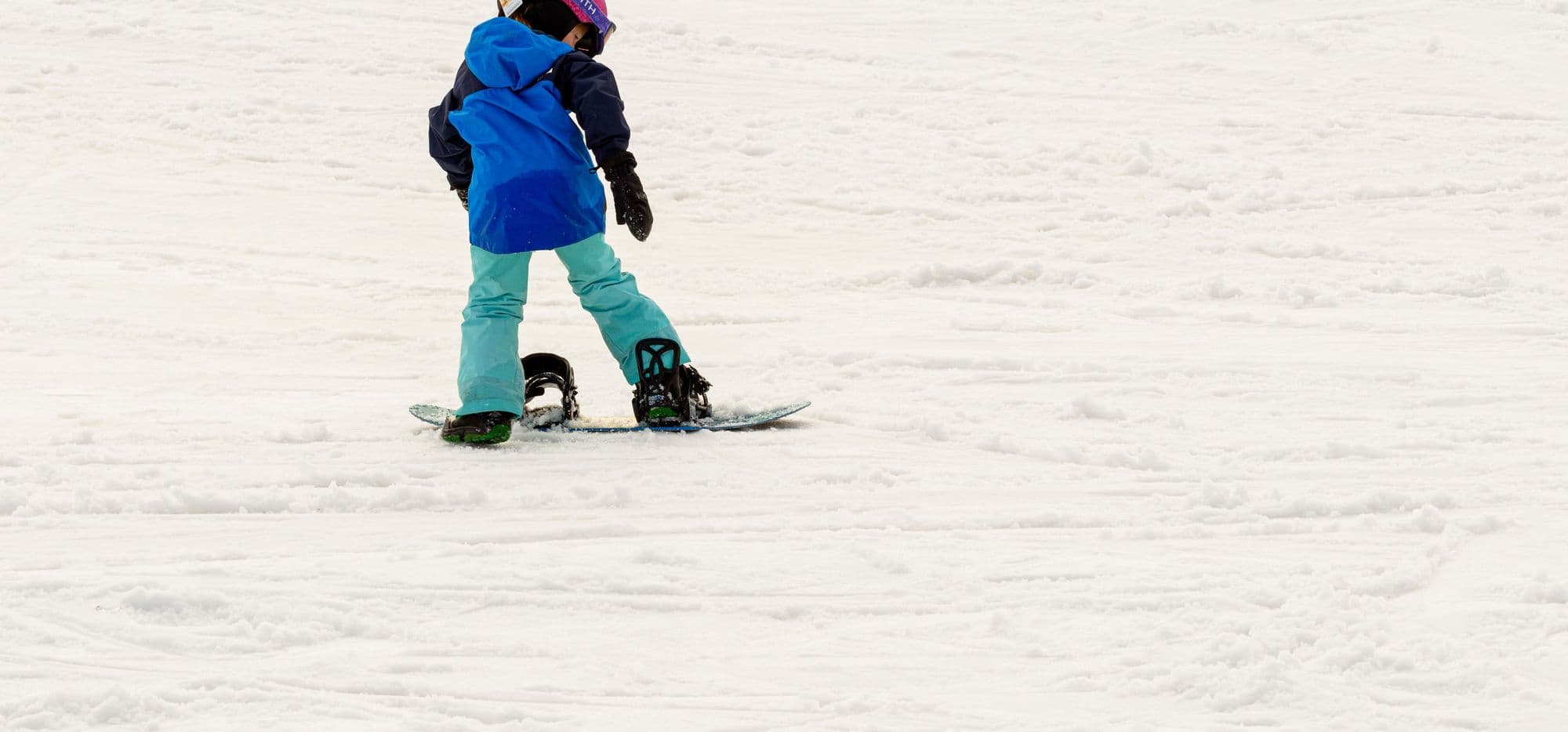 A young snowboarder in a pink helmet riding across fresh snow