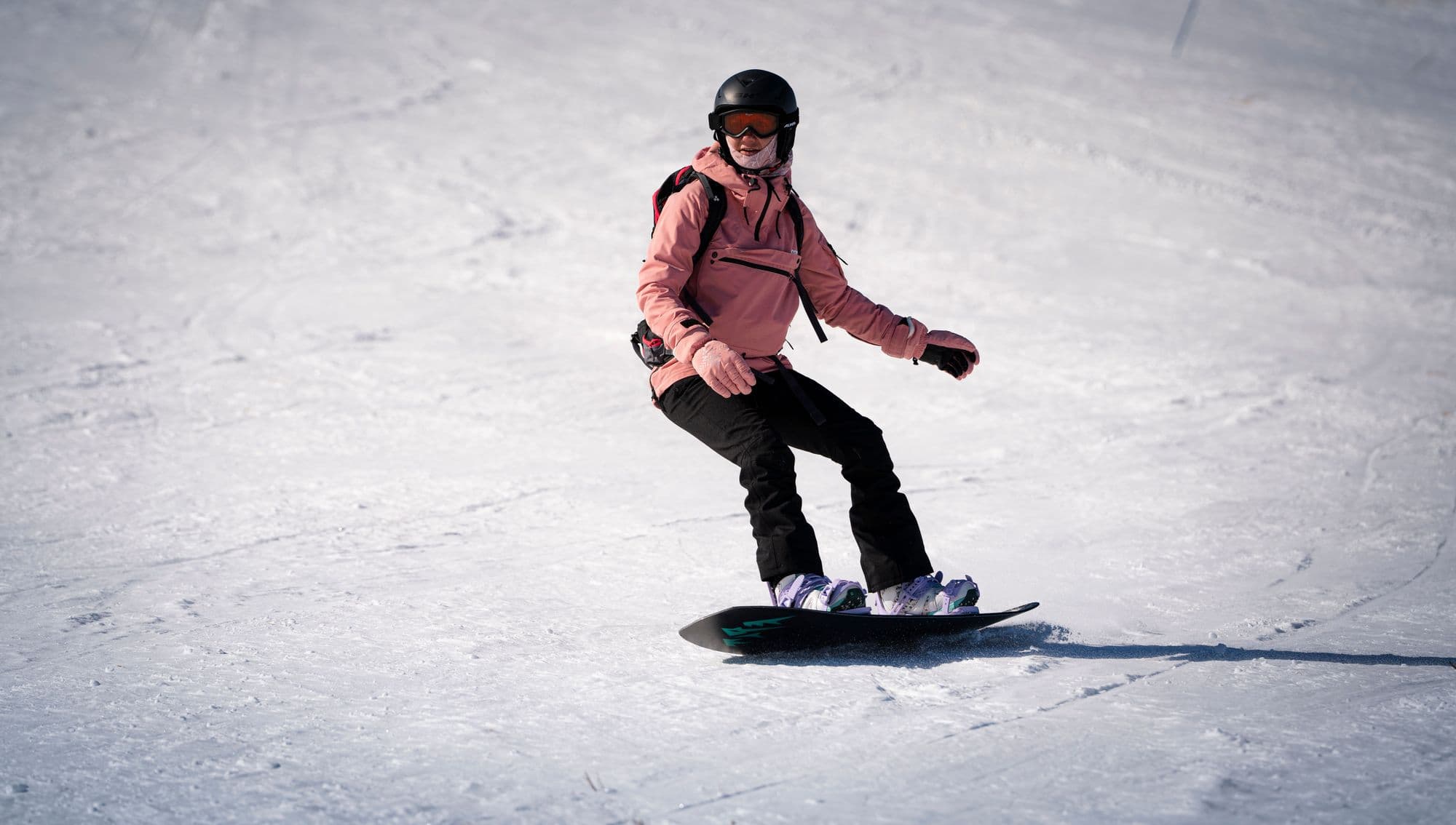 A snowboarder in a pink jacket and helmet riding confidently down a sunny slope