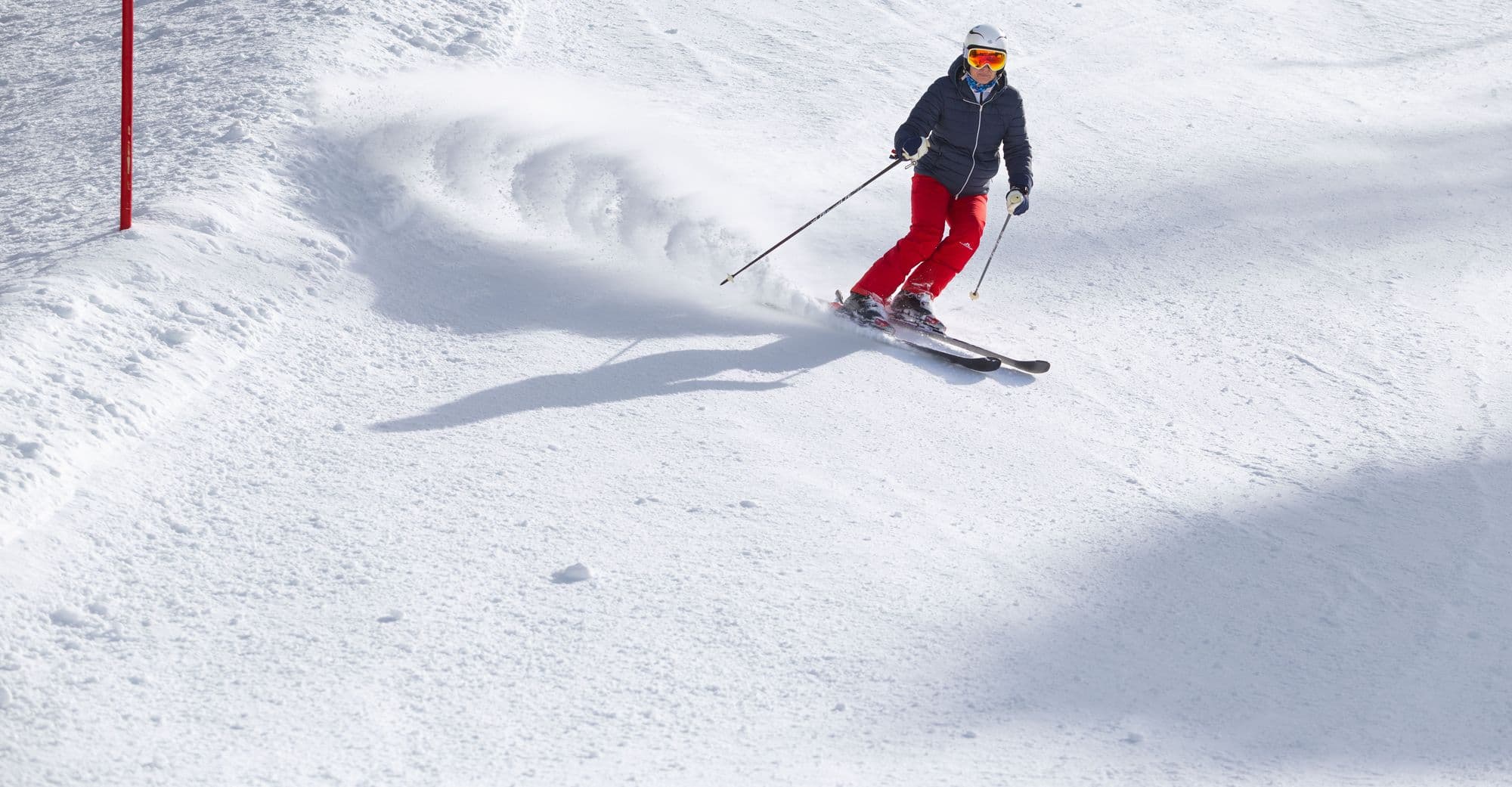 A skier carving across a sunlit mountain slope