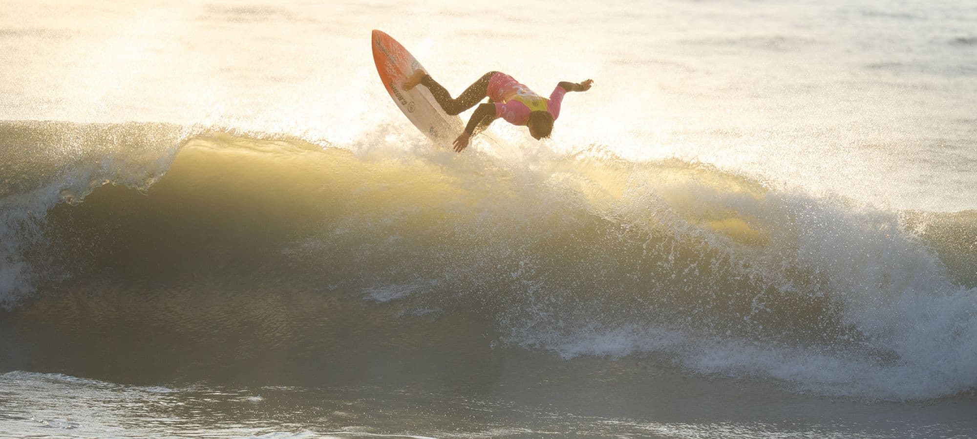 A surfer launching an aerial off a golden sunrise wave