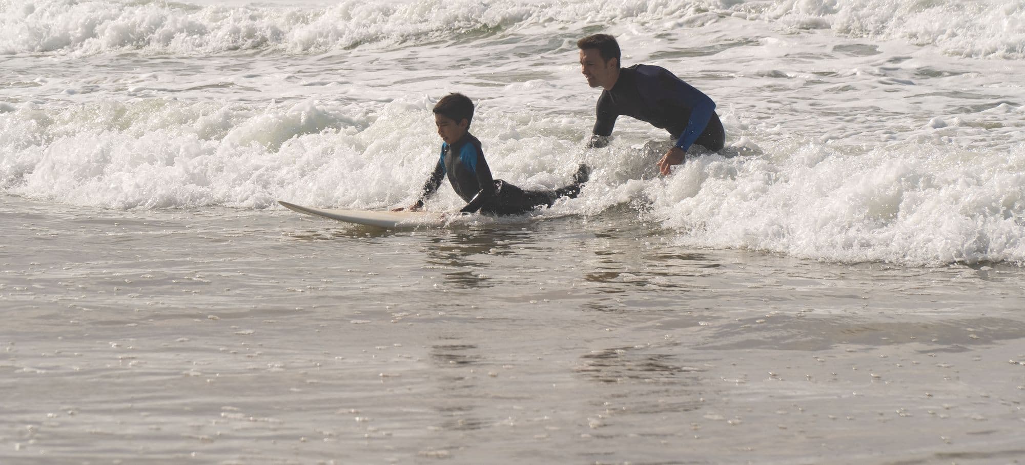 A surf instructor pushing a young beginner into a whitewater wave
