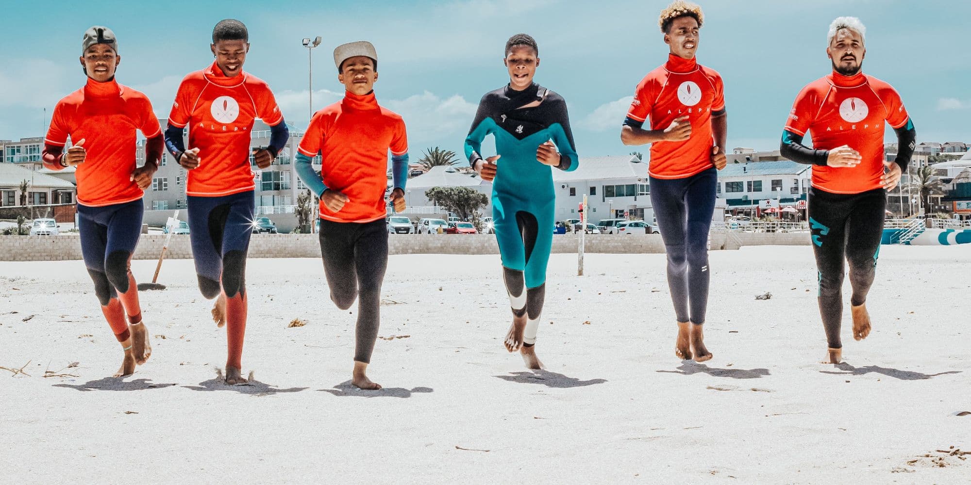A surf school group in matching rash vests running down a sunny beach to the sea