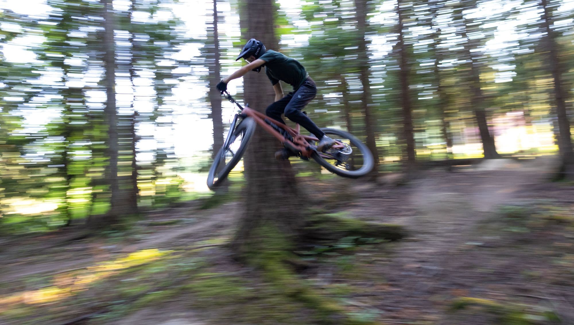A mountain biker in a helmet jumping along a forest trail