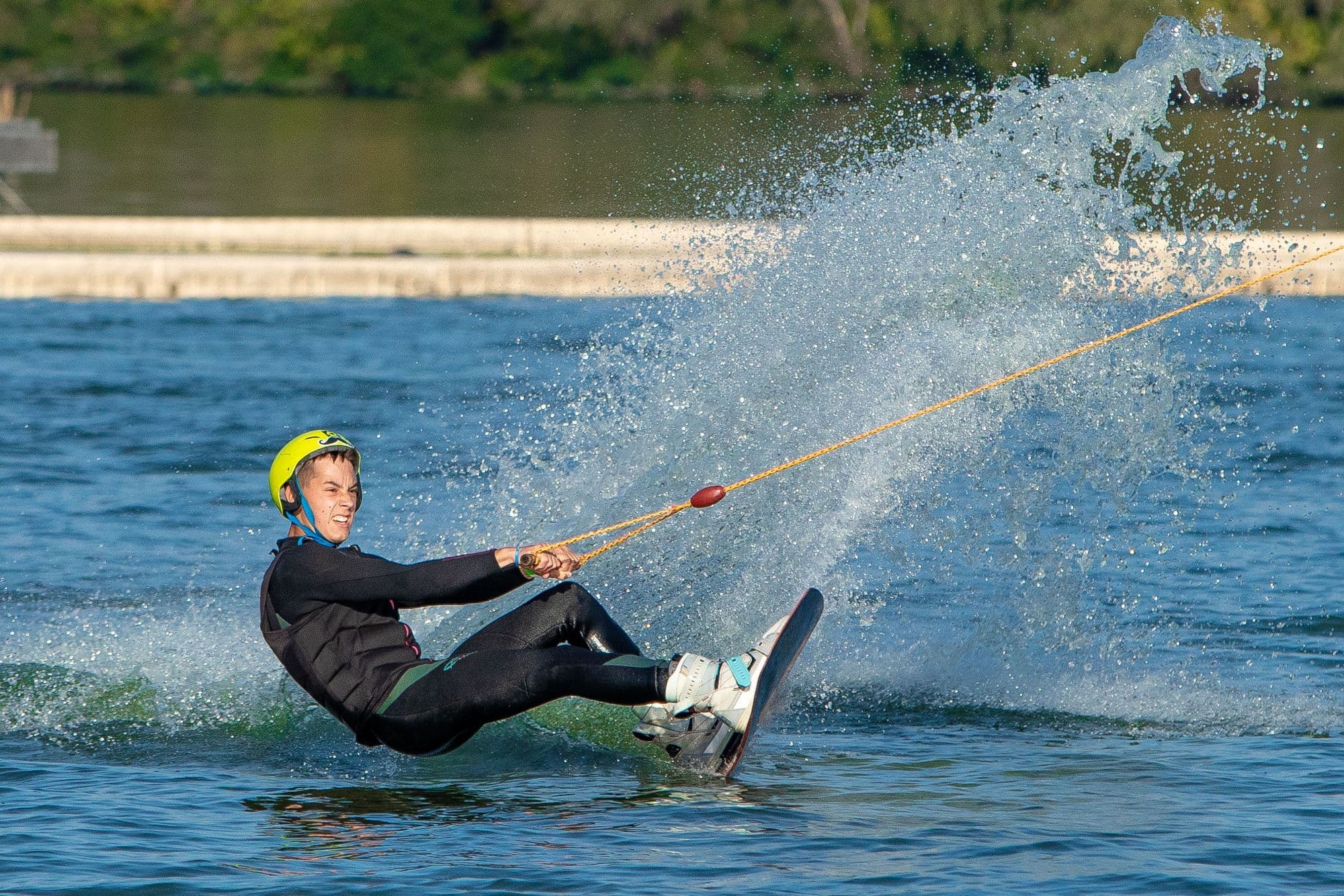 Wakeboarder in helmet and impact vest carving a huge spray