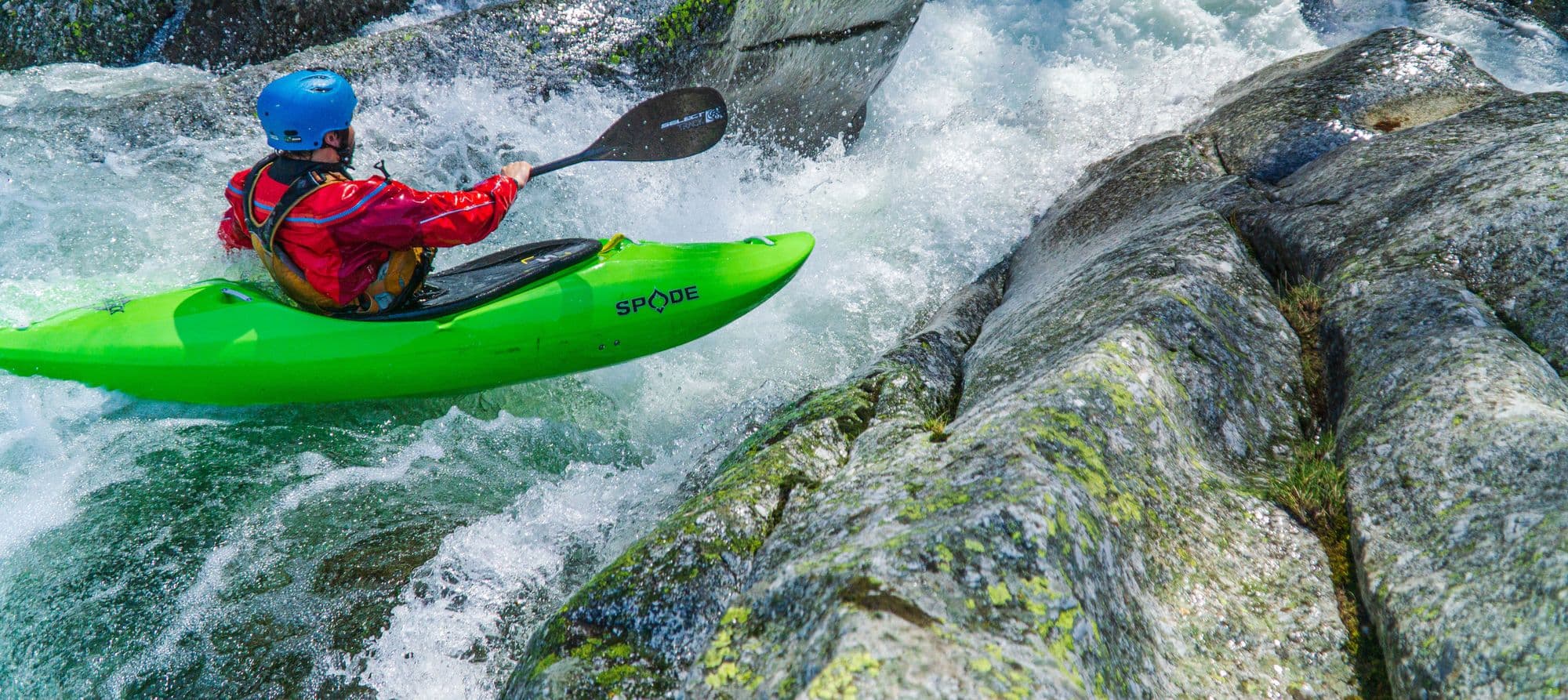 A kayaker in a green boat running a rocky whitewater rapid