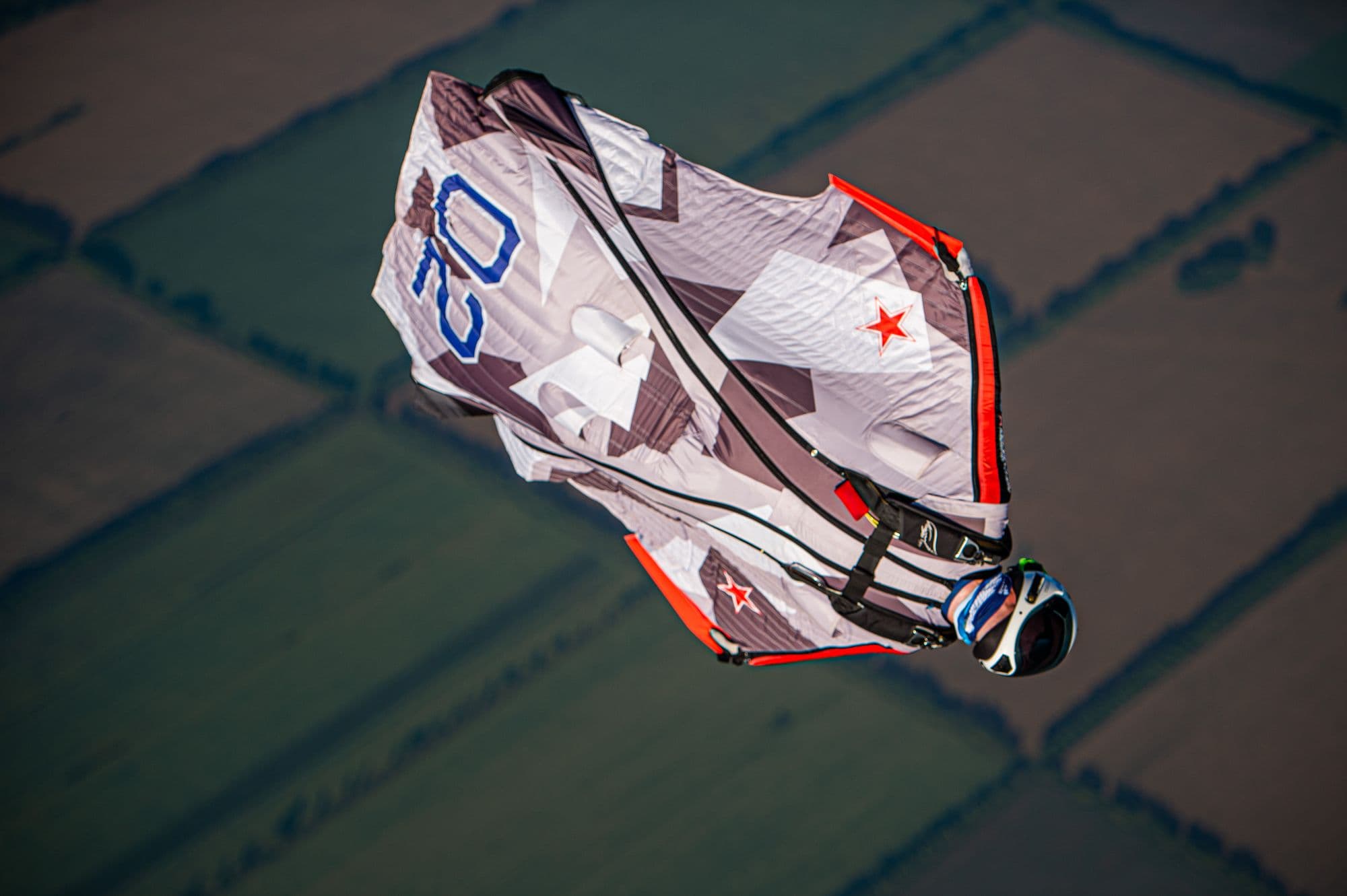 Wingsuit pilot accelerating over farmland during a performance competition round