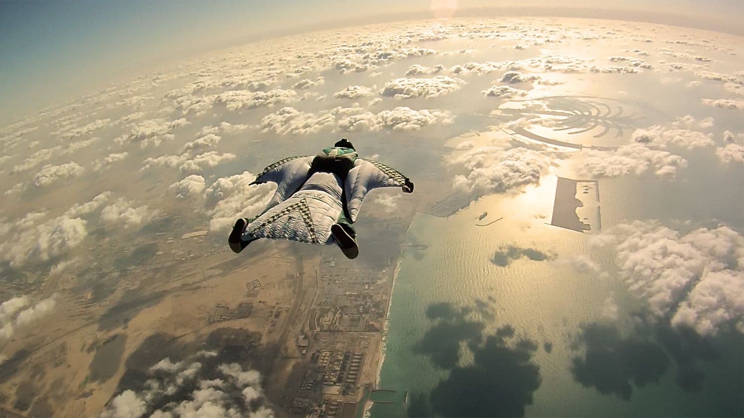 Wingsuit flyer in freefall high above clouds and the coastline