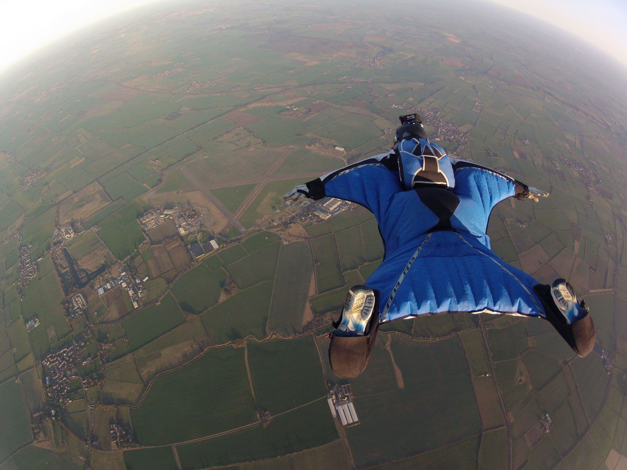 Wingsuit flyer in a blue suit gliding high above the fields around Langar Airfield
