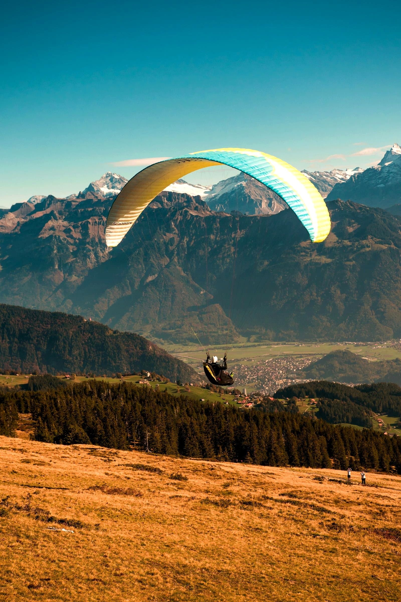 Paraglider with a white, cyan and yellow wing over a mountain valley